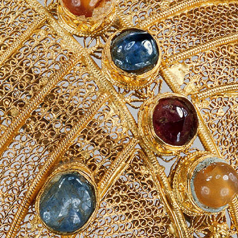Close detail of an imperial gold filigree headdress set with blue, red, and amber cabochon stones.